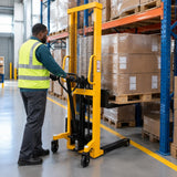 African American warehouse operator using an Atlas manual hydraulic stacker to raise a pallet of cartons toward storage racking