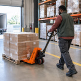 African American stockroom operator steering an Atlas manual pallet truck carrying sealed cartons into a marked storage lane