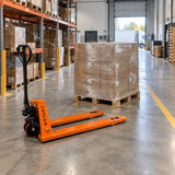 Organised wholesale stockroom with palletised cartons staged for dispatch and an Atlas manual pallet truck resting nearby