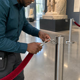 Facilities coordinator attaching an Atlas galvanised snap hook to a light barrier rope in a museum foyer