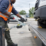 African American recovery technician operating an Atlas ratchet cable puller to move a utility vehicle onto a flatbed platform.