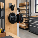 Black Climax behind-the-neck safety earmuff resting on a PPE hook in an organised professional woodworking shop.