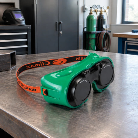 Climax green welding goggles resting on an organised metal-fabrication workbench beside PPE storage