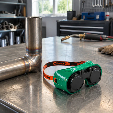 Finished brazed metal assembly with Climax flip-up welding goggles resting beside it on a fabrication bench