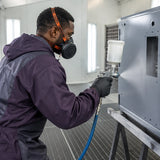 African American spray-finishing technician wearing a Climax CLI-755-A respirator while coating a metal enclosure