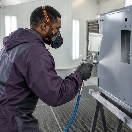 African American spray-finishing technician wearing a Climax CLI-755-A respirator while coating a metal enclosure