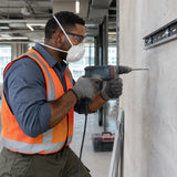 African American maintenance technician wearing a Climax valved FFP2 respirator while drilling concrete anchors indoors