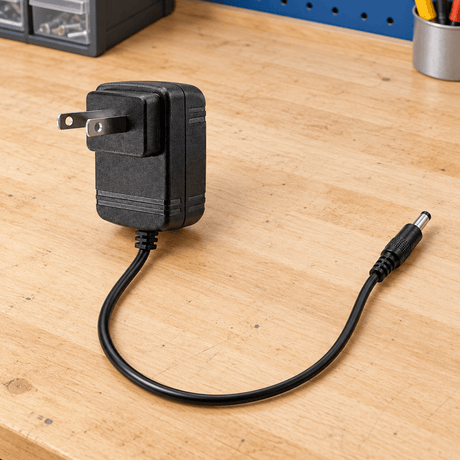 Two-pin power adapter with its full cable visible on a workbench