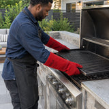 African American adult wearing Irona red leather gauntlet gloves while repositioning a hot grill grate in an outdoor kitchen.
