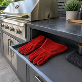 Irona red leather welding gauntlet gloves resting beside a built-in grill in a contemporary outdoor kitchen.