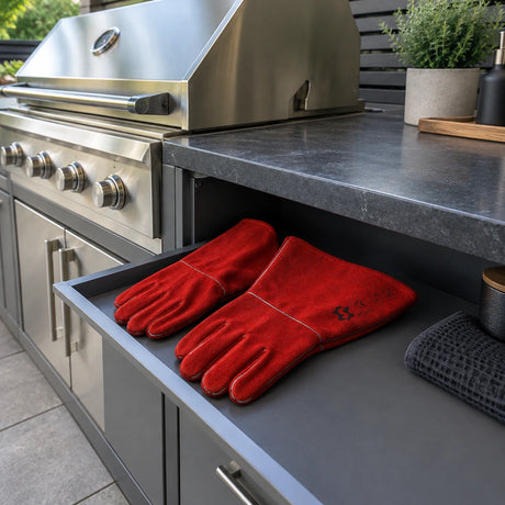 Irona red leather welding gauntlet gloves resting beside a built-in grill in a contemporary outdoor kitchen.