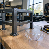 Completed metal frame ready for inspection beside Irona clear safety goggles in an organised workshop.