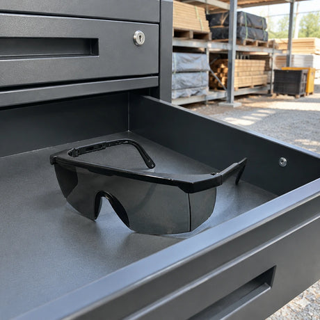 Irona dark-lens safety goggles resting in a PPE drawer at an organised construction material staging area