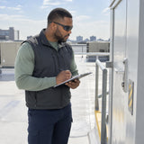 African American facilities technician wearing Irona dark tinted safety goggles while inspecting a bright commercial rooftop service area.