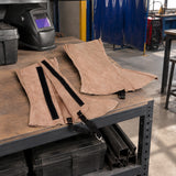 Irona leather welding leggings resting at an organised metal-fabrication workshop PPE station