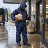 African American delivery worker wearing the Irona navy raincoat and trousers while handling a parcel in the rain.