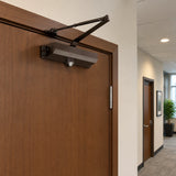 Brown Irona surface-mounted door closer installed on a closed brown office door in a clean corridor