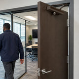 African American facility operator walks away as a brown Irona door closer returns an office door toward closed