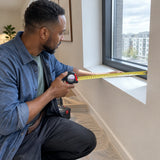 African American interior installer measuring a window recess with a Kyoto red and black metric tape measure