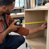 Joiner using a Kyoto 7.5m metric tape measure to measure a cabinet opening in a workshop