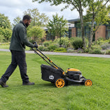 African American groundskeeper guiding a Marsant self-propelled gasoline mower across a broad institutional lawn while collecting clippings