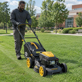 African American groundskeeper guiding a Marsant self-propelled mower across a broad institutional lawn while collecting clippings
