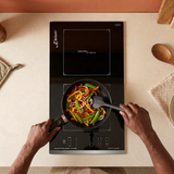 Corrected face-hidden cooking scene with natural hand placement on the black Kaiser Domino induction hob