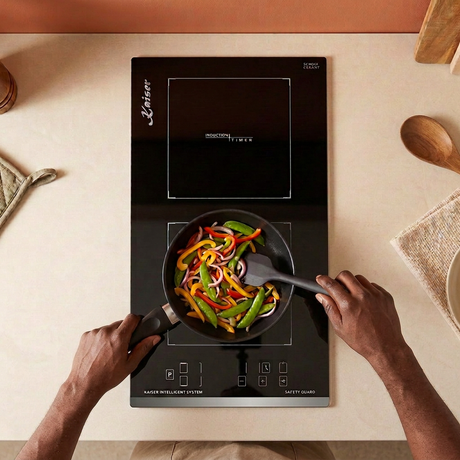 Corrected face-hidden cooking scene with natural hand placement on the black Kaiser Domino induction hob