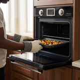 Face-hidden scene loading a tray into the open Kaiser oven