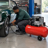 Automotive technician uses a Mirage 2HP 50L air compressor to inflate a classic car tyre in a clean workshop.