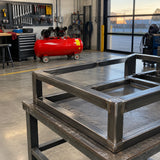 Finished steel frame on an inspection stand with the inactive Mirage 300L air compressor ready in the fabrication shop.