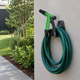 Green adjustable garden spray gun resting on a hose hanger beside a neatly maintained residential garden