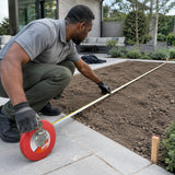 Landscape installer using a red Mister 20m open-reel tape to measure a courtyard planting bed.