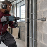 African American building-services installer using the Mister SDS-Plus extension adapter with a rotary hammer to drill a deep blockwork opening.