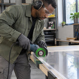 African American installer uses a compatible guarded grinder fitted with the NRG 115mm diamond disc to cut a supported rigid plastic panel.
