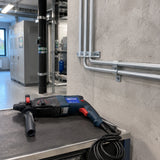 Completed conduit support anchored to a concrete plant-room wall with the Pirana rotary hammer resting nearby.