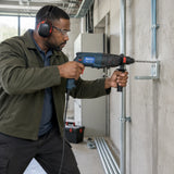 Building-services installer using a Pirana rotary hammer to drill an anchor hole in a concrete plant-room wall.