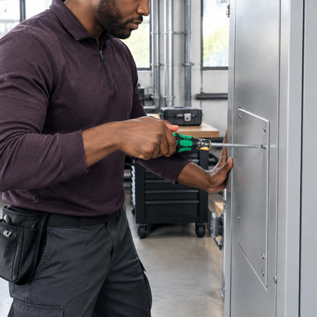 African American facilities technician tightening a slotted service-cover screw with a Wera 334 screwdriver.