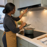 African American home cook checking a simmering pot beneath the Kaiser EA 644 Eco built-in cooker hood in a refined condominium kitchen.