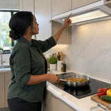 African American home cook using the Kaiser EA 946 W Eco cooker hood while sautéing vegetables in a modern kitchen.