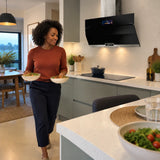 Finished bowls are carried through a calm contemporary kitchen after cooking beneath the Kaiser La Perle black glass cooker hood.