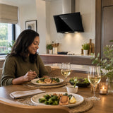 Finished dinner in a calm open-plan kitchen with the Kaiser black glass cooker hood visible above the cleared cooking area.