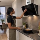 African American home cook adjusts the Kaiser black glass cooker hood while pan-searing dinner in a contemporary kitchen.
