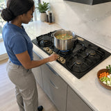 African American home cook adjusts the Kaiser five-burner gas hob while simmering vegetable stock in a stockpot
