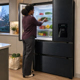 African American adult organising fresh groceries on the glass shelves of a Kaiser black stainless steel French-door refrigerator.