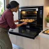 African American home cook loading a tray of savoury pastries into the open Kaiser EH 9309 wide electric oven