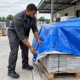 African American materials handler pulling a Wadfow 7 × 10 m blue tarp over a pallet of construction supplies