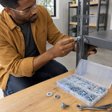 African American adult selecting flat and lock washers from the Wadfow WVW1B01 kit for a steel shelf bracket in a home utility room