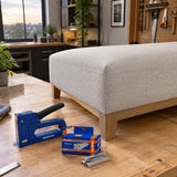 Finished textile-covered wood panel with Wadfow WNA0810 staple pack and compatible staple gun in a repair studio.