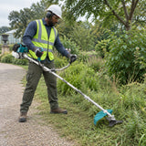 African American grounds worker using the Total TP5524421 brush cutter with its three-tooth blade along a botanical garden path
